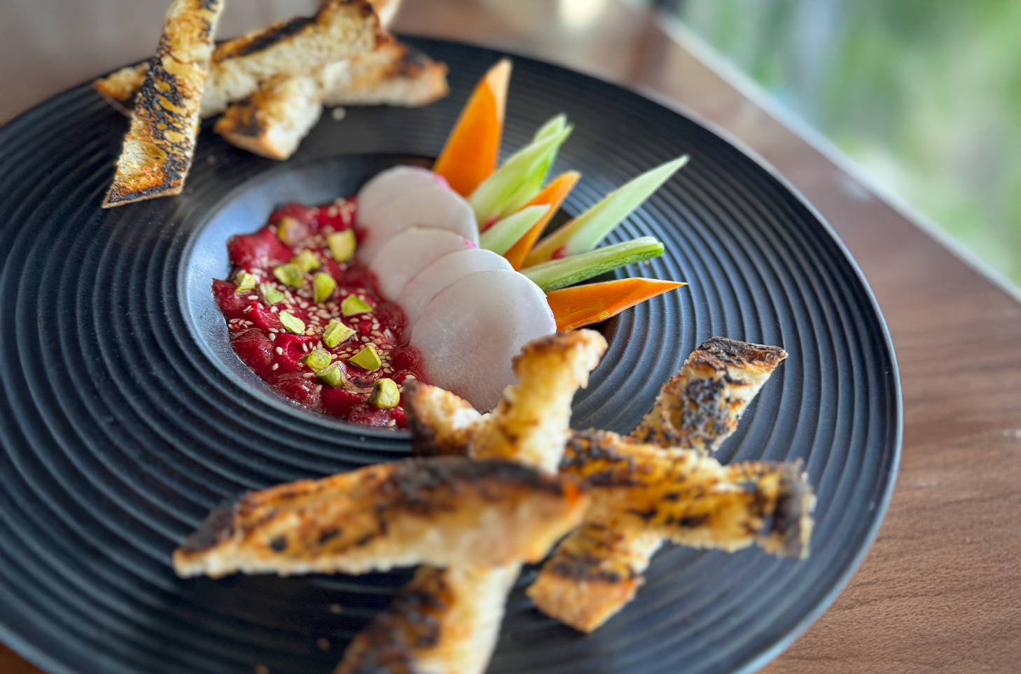 beet hummus with crostini in a black ceramic bowl