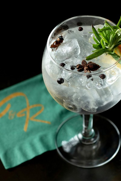 A Gin and Tonic on a green napkin with a rosemary sprig garnish